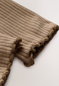 Tissu beige côtelé avec un bord ondulé et froncé. Texture douce, design léger. Les détails des coutures sont subtils, améliorant l'aspect général.