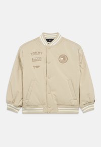 Giubbotto bomber beige con bottoni a pressione, polsini e orlo a coste. Presenta loghi stampati sul petto e sulle maniche, realizzato in tessuto liscio.