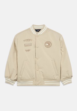 Bežinė bomber tipo striukė su snap mygtukais, raukšlėmis ant rankovių ir apačios. Įrengta spausdintomis logotipų ant krūtinės ir rankovių, pagaminta iš glotnaus audinio.