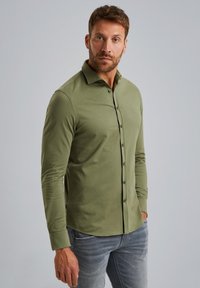 Olijfgroene overhemd met lange mouwen en een button-down kraag, voorzien van een voorkant met zwarte knopen en subtiele branding op de borst.