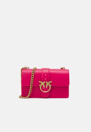 Sac à main en cuir rose vif avec une bandoulière chaîne dorée et un fermoir doré orné de deux oiseaux se faisant face sur un fond clair.