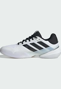 Άσπρο αθλητικό παπούτσι με μαύρες λεπτομέρειες, διαθέτοντας υφασμένο επάνω μέρος, τρεις χαρακτηριστικές ρίγες και ανθεκτική, υφή σόλα.