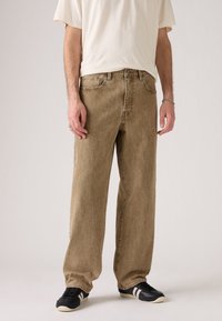 Beige denim jeans met een relaxte pasvorm, vervaagde textuur, vijf-pocket ontwerp en subtiele stikseldetails, gecombineerd met zwarte sneakers.