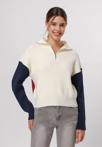 Maglione a maglia con mezza zip, caratterizzato da un corpo crema, maniche blu navy e rosse, texture a coste e orlo aderente.