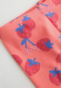 Gros plan sur un tissu côtelé rose avec un motif de grandes fraises rouges et de petites cerises rose clair avec des feuilles bleues.