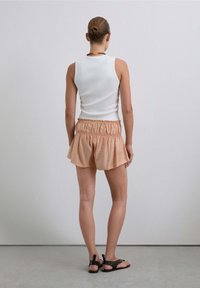 Top sin mangas de canalé blanco combinado con pantalones cortos sueltos de color melocotón que tienen una cinturilla elástica y un dobladillo con volantes, junto con sandalias marrones.