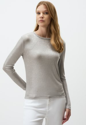 Top argentato a maniche lunghe con una texture liscia e scollatura rotonda, abbinato a pantaloni bianchi con una vestibilità attillata.