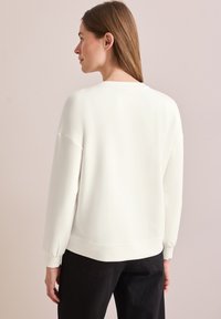 Felpa bianca leggera con un fit rilassato, maniche lunghe e polsini a costine. Texture liscia, design semplice e scollatura a girocollo.