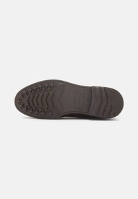Suela de zapato marrón oscuro con goma texturizada, que presenta patrones de estrellas y rayas, detalles del logo y un diseño plano y duradero.