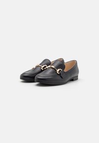 Zwarte leren loafers met een gladde textuur, puntige neus en hardware accenten in goudkleur over de wreef. Laag, plat hakontwerp.