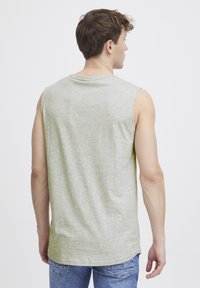 Mouwloze, lichtgrijze katoenen t-shirt met een ronde hals en een losse fit, gedragen met blauwe spijkerbroek. Zachte textuur, casual ontwerp, geen zichtbare patronen.