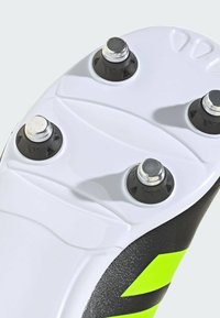Suola di scarpini da calcio neri e giallo neon con sei tacchetti sostituibili, superficie bianca texturizzata e forma aerodinamica per una presa ottimale.