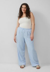 Lichtblauw en wit gestreepte wijde broek met een elastische tailleband en een trekkoord. Model draagt een strakke witte tanktop en sandalen.