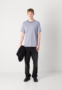 Lys grå kortærmet T-shirt med en sort ribbet halsudskæring, parret med sorte jeans og sorte sneakers, båret med en sort jakke.