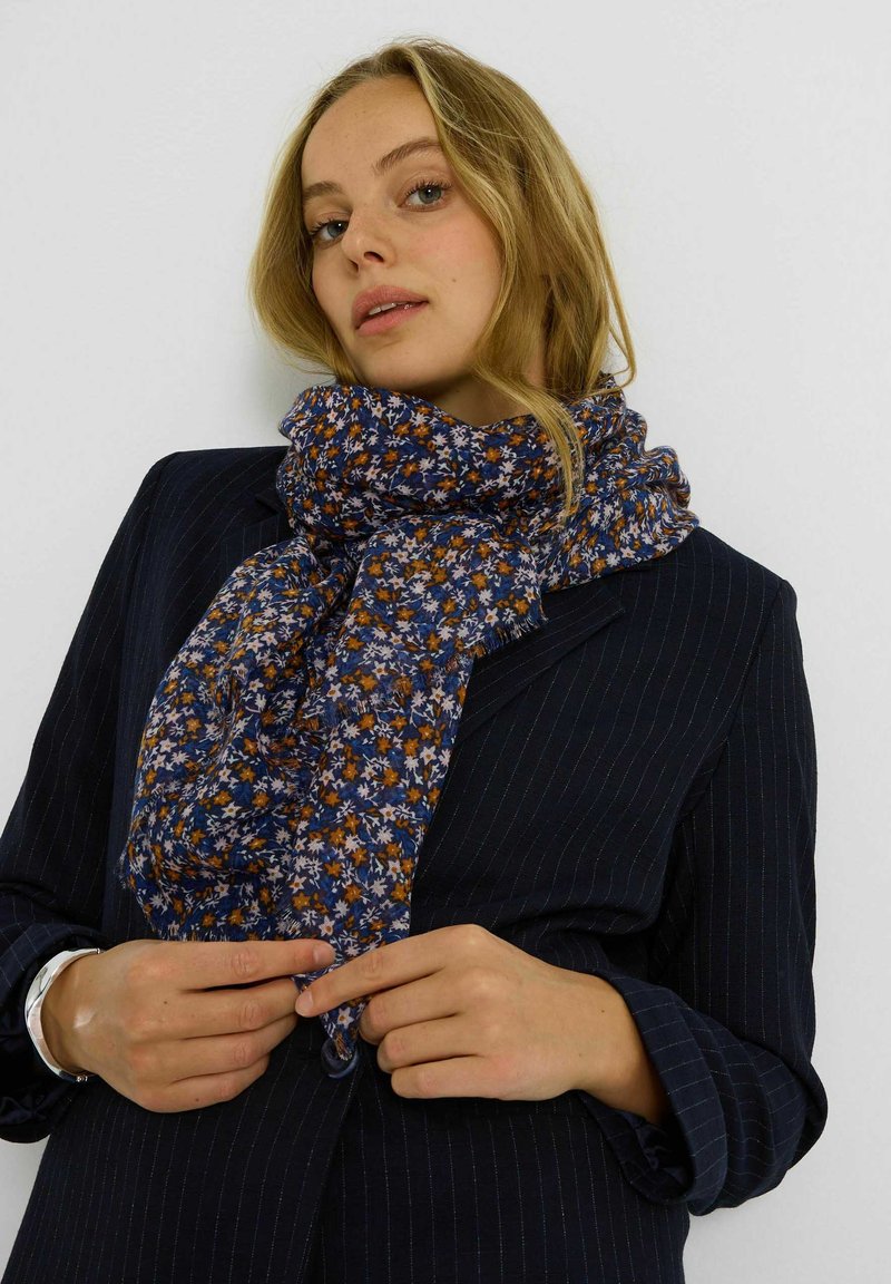 Pañuelo con estampado floral en azul marino con flores naranjas y blancas, hecho de tela ligera, envuelto alrededor del cuello, cayendo suavemente.