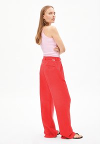 Rode broek met wijde pijpen en een losse pasvorm, voorzien van een taille met riem en een achterzakdetail, gecombineerd met een strakke roze tanktop.