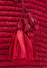 Czerwona pleciona torebka na ramię z fakturowaną powierzchnią, skórzanymi frędzlami i zaokrąglonym dnem; wykonana z materiałów syntetycznych.