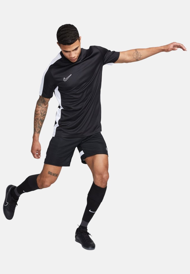 Maglia atletica nera con accenti bianchi ai lati, abbinata a pantaloni corti neri. La maglietta presenta un colletto rotondo e il logo Nike sul petto.