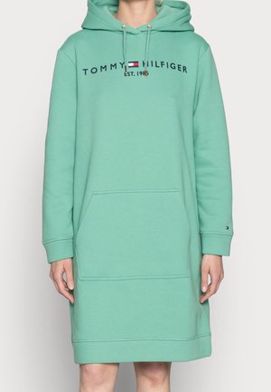 Personne portant une robe à capuche Tommy Hilfiger vert menthe avec une poche avant et un logo sur la poitrine.