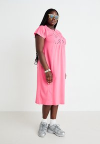 Vestido midi de algodão rosa com mangas curtas, detalhe de bordado na frente e corte descontraído, combinado com ténis prateados e óculos de sol.