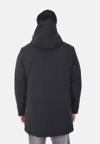Parka nera lunga con cappuccio, dalla finitura opaca e liscia. Presenta un colletto alto, tasche laterali e un design dritto. Stile minimalista.