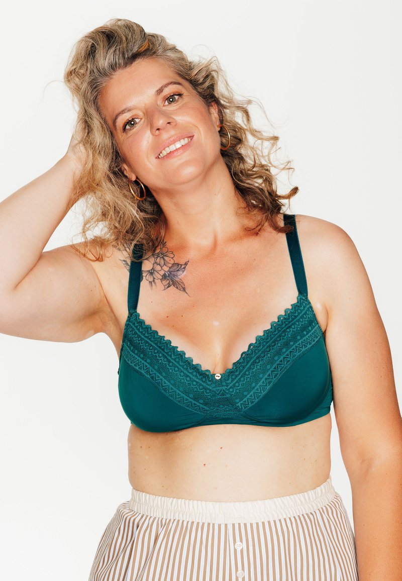 Bralette teal con rifiniture in pizzo e design a V, caratterizzato da bordi scallop, un pulsante decorativo e spalline larghe, abbinato a pantaloni a righe.