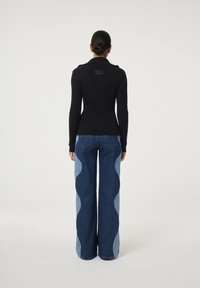 Zwarte geribbelde trui met een hoge kraag, gecombineerd met lichtblauwe flared jeans met contrasterende lichtblauwe golfpatronen.