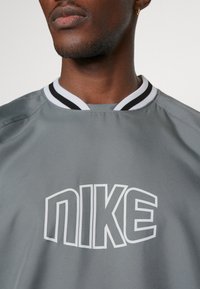 Maglietta sportiva grigia con logo Nike bianco. Il collo ha righe bianche e nere. Realizzata in tessuto leggero e morbido.