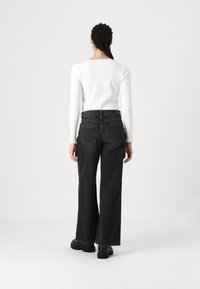 Black wide-leg jeans with a high waistband and two back pockets, paired with a fitted white ribbed long-sleeve top.
