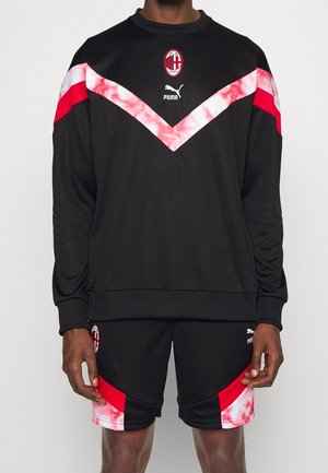 Sort sportstøj med rødt og hvidt chevronmønster, AC Milan- og Puma-logoer, bestående af langærmet overdel og matchende shorts.