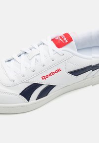 Fehér sneaker tengerészkék részletekkel, bőr anyagból, lapos fehér fűzőkkel, piros Reebok logóval a nyelvén, párnázott belsővel.