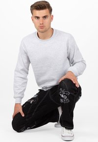 Felpa grigia a collo rotondo con polsini a coste, abbinata a jeans neri ricamati con tasca con zip e sneakers bianche con dettagli rossi.