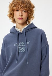 Granatowy hoodie z dużym nadrukiem z przodu, przedstawiającym "New York City Music Festival" oraz wzór zestawu perkusyjnego, wykonany z miękkiego materiału, z ściągaczami.