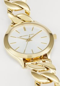 Gouden Michael Kors horloge met een glanzende witte wijzerplaat, voorzien van een chunky schakeltjes armband en minimalistische uurmarkers.