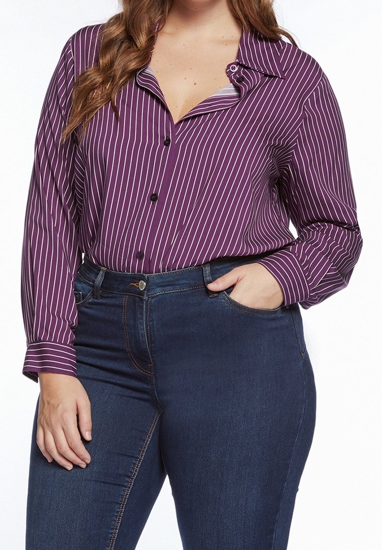 Fialová košile na knoflíky s bílými vertikálními pruhy, dlouhými rukávy a límečkem. Nosená s tmavě modrými upnutými džínami, které mají přední kapsu.