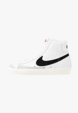 High-top white sneakers with black accents, suede toe cap, textured rubber sole, and visible stitching on a smooth leather upper.