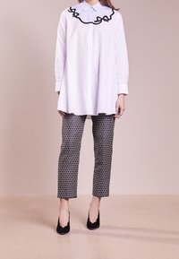 Biała koszula z długim rękawem z czarnymi falbanami i niebieską warstwą z kołnierzykiem, połączona z dopasowanymi spodniami w czarno-białe wzory oraz czarnymi szpilkami.