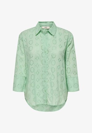 Light green blouse with a button-down front, three-quarter sleeves, and floral eyelet patterns throughout. Soft, textured cotton fabric.