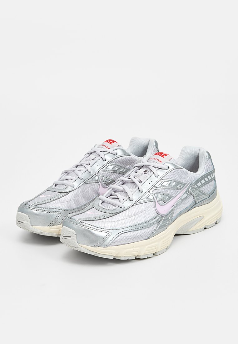 Zapatillas deportivas plateadas con materiales de malla y sintéticos, que presentan acentos rosas, un diseño texturizado y una suela de goma blanca.