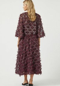 Bourgognefarvet lagdelt kjole med frynsebesætning, korte ærmer og en flydende silhuet. Gennemsigtigt stof med bølgede mønstre.