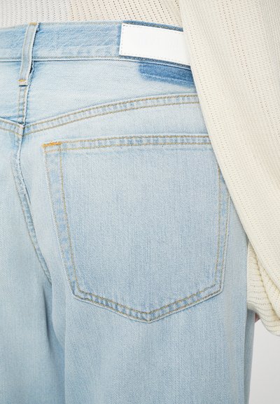 Jeans in denim azzurro chiaro con un classico design a cinque tasche, cuciture gialle e un'etichetta bianca in vita. Texture liscia.