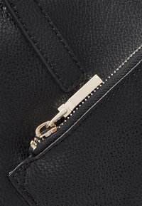 Portefeuille en cuir noir avec une finition texturée, présentant une quincaillerie à fermeture éclair en ton doré et un détail de rabat rectangulaire. Bord de la fermeture éclair mis en valeur.