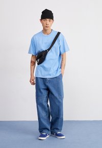 Ανοιχτό μπλε βαμβακερό T-shirt με μικρό λογότυπο, μαύρη μέση τσάντα, χαλα�ρούς τζιν και μπλε αθλητικά παπούτσια. Μινιμαλιστικός σχεδιασμός με άνετη εφαρμογή.