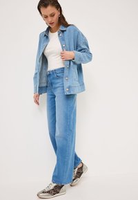 Veste en denim bleu clair sur un haut blanc, assortie à un jean bleu clair et des baskets avec accents argentés présentant un imprimé léopard.