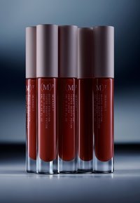 Viisi sylinterimäistä huuliväriputkea, joissa on vaaleanpunaiset korkit, läpinäkyvät lasirunkoiset ja syvänpunainen neste näkyvissä, valkoisella tekstillä merkitty.