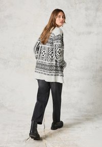 Stickad tröja i svart och vitt mönster, med geometriska designer, långa ärmar och en lös passform, ihop med mörka, avkopplande jeans.