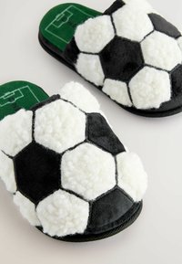 Sort-hvide, fluffy tøfler formet som en fodbold, med hexagonale mønstre, blød tekstur og en grøn indersål med et grafik af et mål.