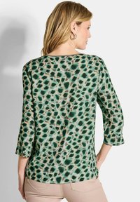 Blusa verde e crema con motivo leopardato, maniche a tre quarti e vestibilità rilassata. Tessuto liscio con leggero lucido.