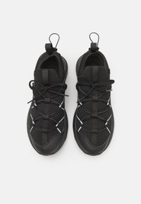 Ett par svarta träningssneakers med snörning, dragflikar på hälen och vit reflekterande detaljering på vit bakgrund.