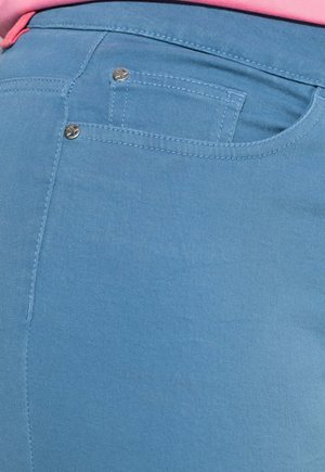 Hellblaue Jeans aus Denim mit glatter Textur, ausgestattet mit einer Gesäßtasche und silberfarbenen Metallakzenten, die Nahtdetails zeigen.